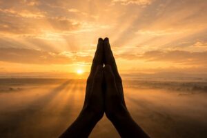 Monday prayers and blessings image - folded hands in prayer against a golden Monday sunrise