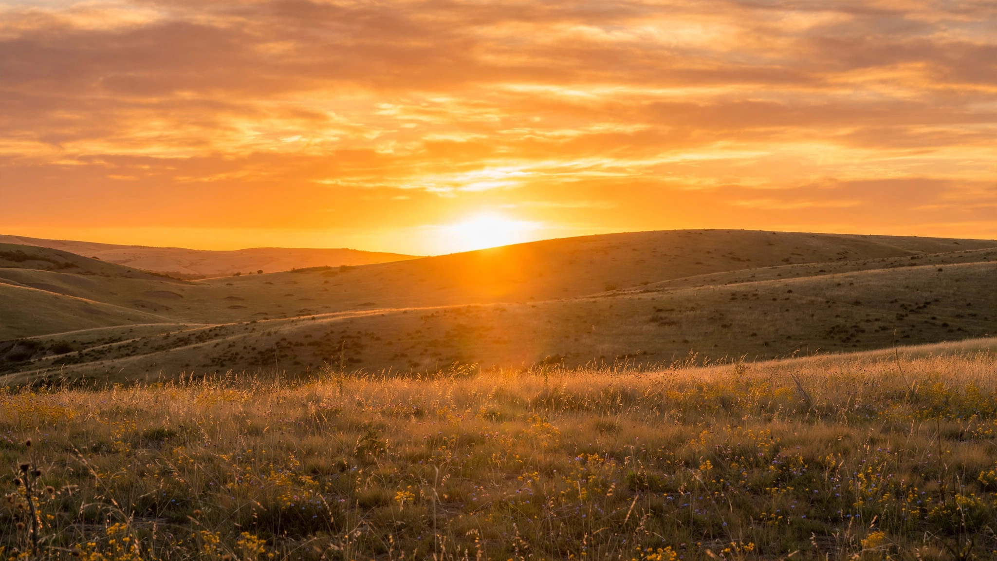 Calm Sunday evening sunset over gentle hills with a warm orange and gold sky